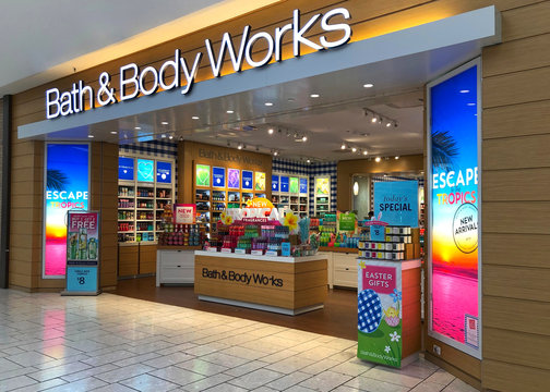 Exterior of a store in a mall, displaying bright promotional posters and shelves filled with body care products and seasonal gifts.