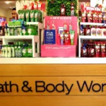 A Bath and Body Works store display showcasing various scented body care products, including lotions and sprays, with a promotional sign highlighting new scents and special offers.