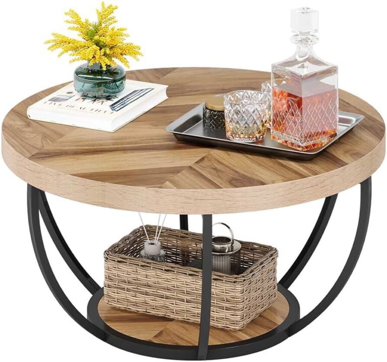 Round wooden coffee table with a black metal base, featuring a decorative tray with a crystal decanter and glasses, along with a book and vase of yellow flowers. A wicker basket is stored on the lower shelf beneath the table.