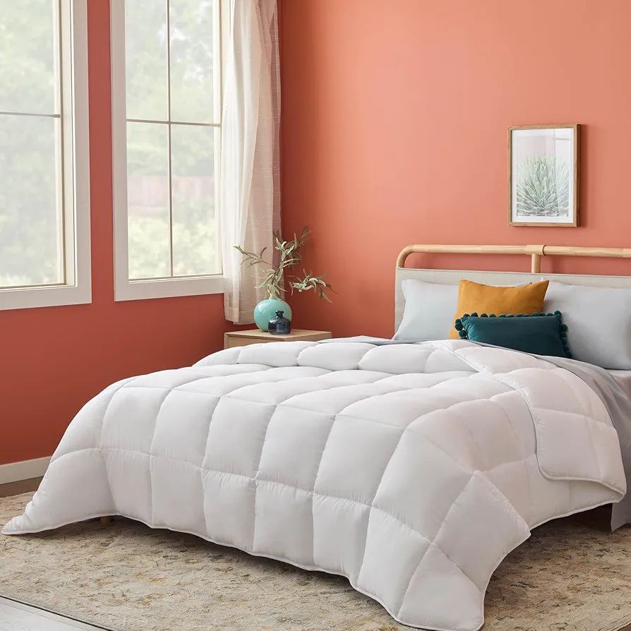 Cozy bedroom with a white quilted duvet on a modern bed against a warm orange accent wall. Decorative pillows and soft natural light enhance the serene setting. Shop Duvet On Sale.