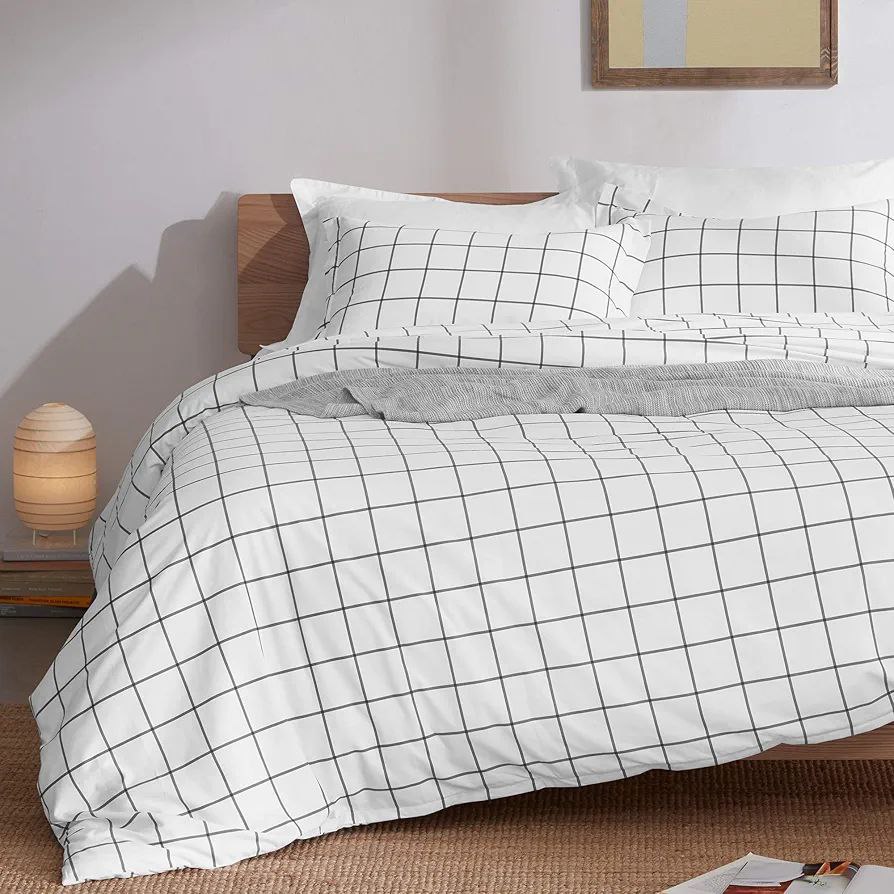 Minimalist bedroom with a white duvet featuring a black grid pattern, paired with matching pillows and soft lighting. Ideal for those looking to shop a stylish duvet on sale.