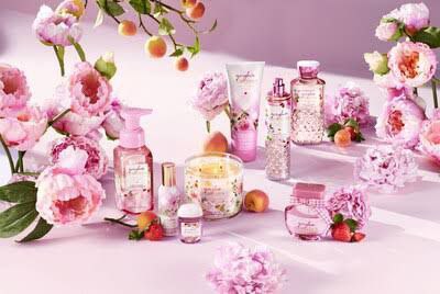 Bath and Body Works floral collection of body care and home fragrance products arranged with pink peonies and fresh fruit, creating a soft and inviting display.