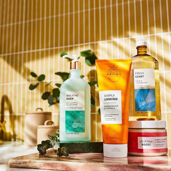 Bath and Body Works Aroma collection featuring Breathe Deep eucalyptus lotion, Simply Unwind sandalwood and vanilla cream, Fresh Start sea salt shower gel, and Uplifting Boost body scrub, displayed with natural decor.