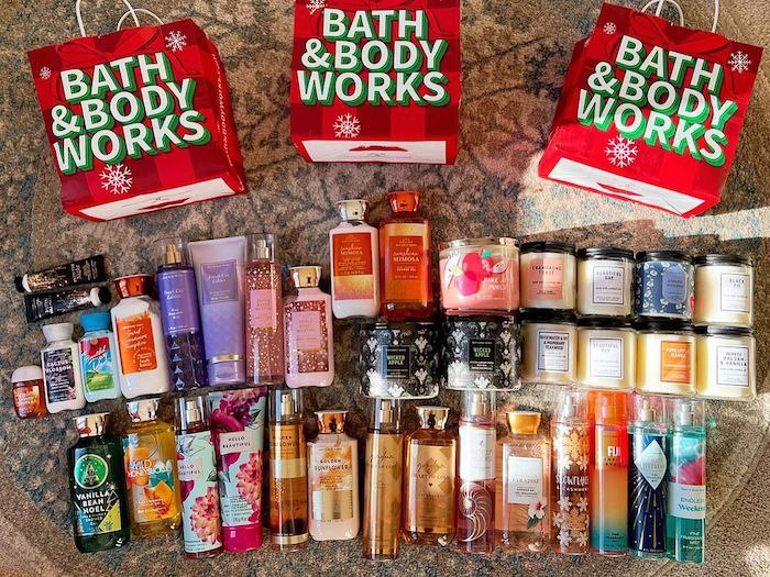 A large Bath and Body Works collection featuring body lotions, fragrance mists, candles, hand sanitizers, and body creams arranged with holiday-themed Bath and Body Works shopping bags.