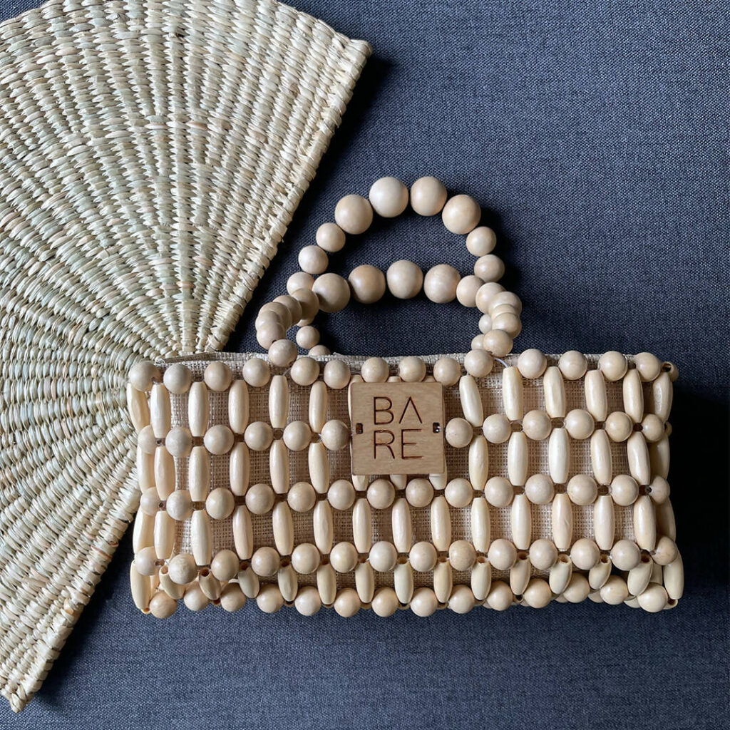 Natural wooden beaded handbag with round and oval beads, featuring a minimalist design and a BARE logo accent, styled on a woven mat for a rustic, eco-friendly look.